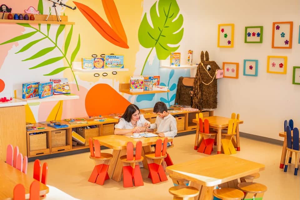 Colorful kids' playroom with wooden furniture, wall art, tropical plant decorations, and vibrant toys