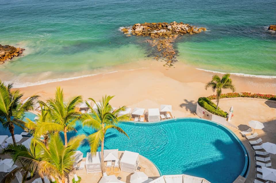 Beachfront resort pool overlooking turquoise ocean, white loungers, and pristine sandy beach