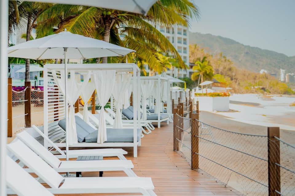 Beachfront white cabanas with umbrellas and loungers on wooden deck with mountain backdrop