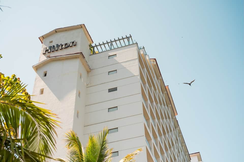 Hilton hotel tower exterior with white facade, multiple floors, and palm trees against blue sky