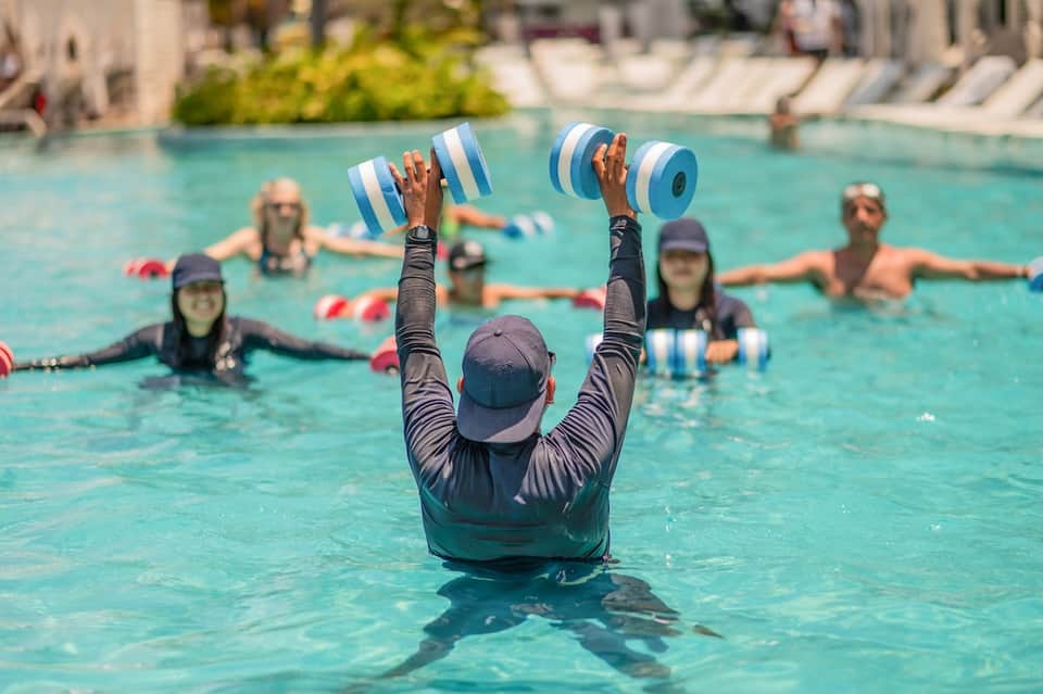 Swim instructor leading group fitness class in pool using blue foam dumbbells
