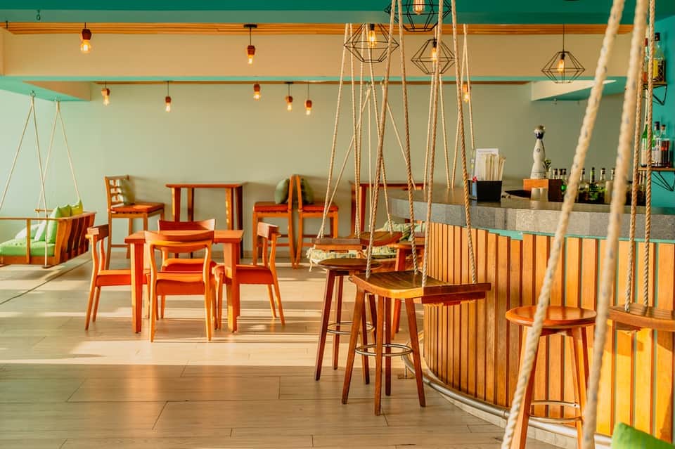 Colorful modern lounge bar with turquoise walls, orange furniture, rope swings, and geometric pendant lights