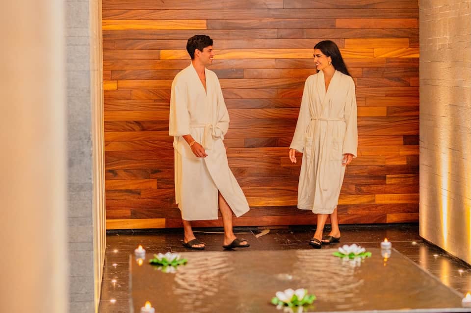 Two women in spa robes standing in wellness area with wooden walls and candles