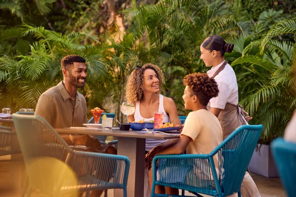 Guests dining outdoors surrounded by lush tropical palm fronds at resort restaurant