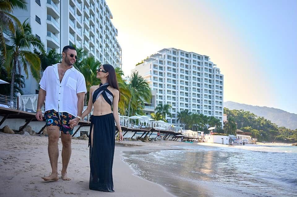 Beach resort setting with couple on sand, high-rise hotel buildings, palm trees, and ocean view