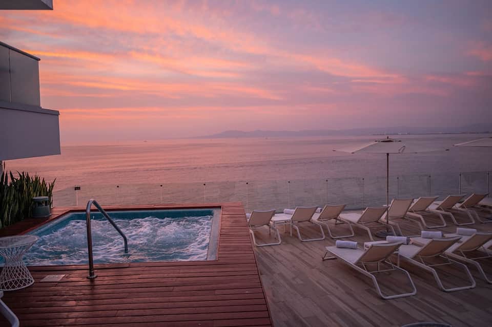 Waterfront resort deck at sunset with infinity pool, lounge chairs, and pink-orange sky