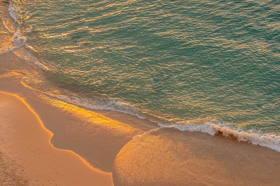 Golden hour beach scene with gentle waves, turquoise water, and pristine sandy shoreline