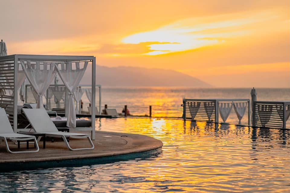 Sunset view of infinity pool with cabanas and ocean horizon at dusk