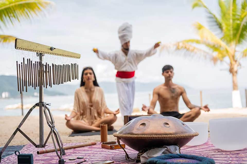 Beach wellness retreat with yoga instructor and participants, meditation gong, ocean backdrop