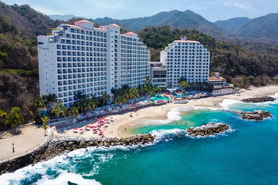 Beachfront resort complex nestled between mountains with sandy beach and turquoise water