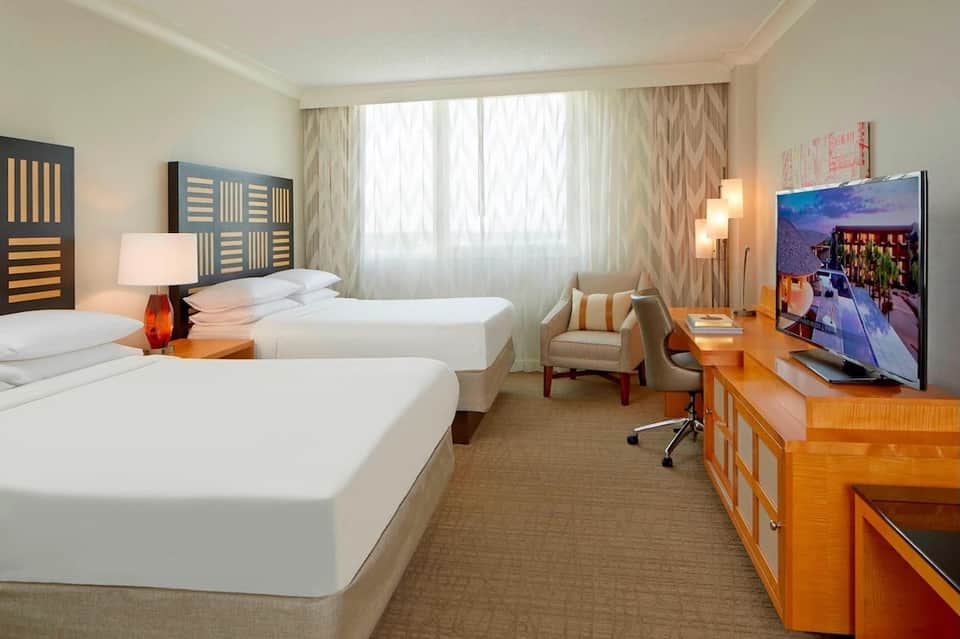 Hotel room with two beds, modern furnishings, TV, seating area, and large windows