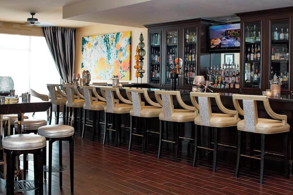 Upscale hotel bar with dark cabinetry, wooden countertop, and extensive liquor collection