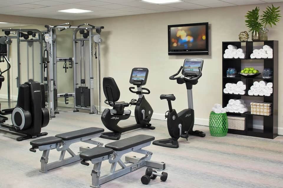 Compact fitness room with exercise machines, stationary bikes, weight benches, and towel storage shelving