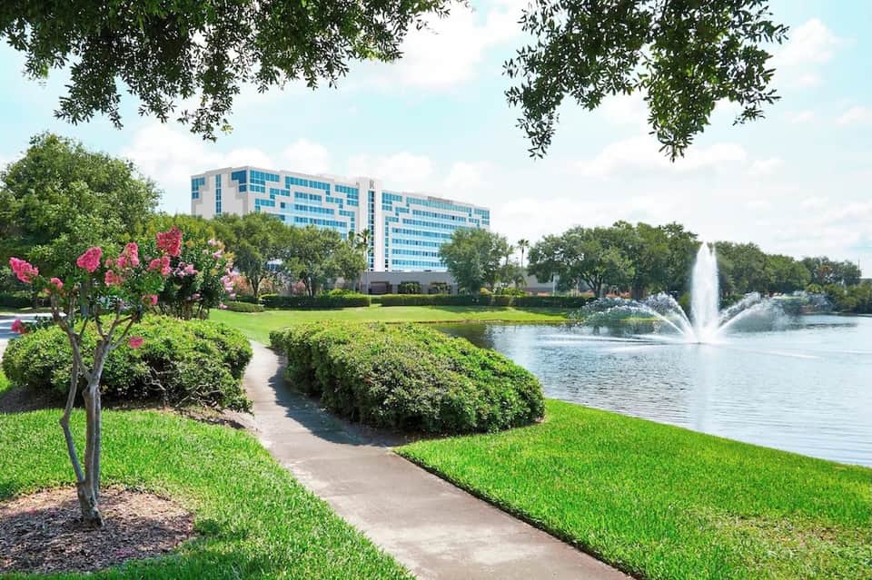 Lakefront resort building with landscaped grounds, flowering trees, and water fountain