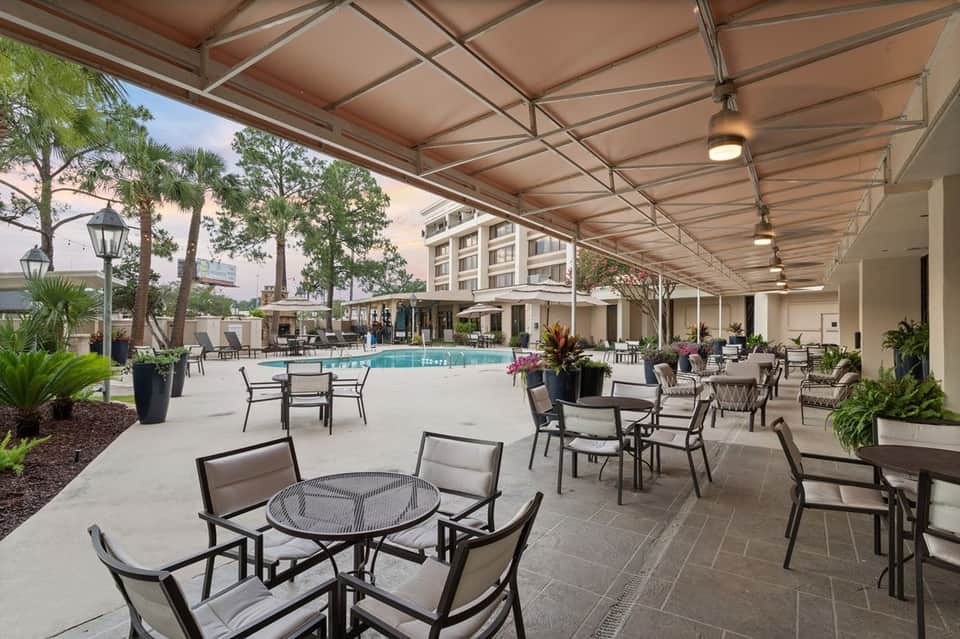 Covered pool patio with modern retractable shade, seating areas, and resort building backdrop