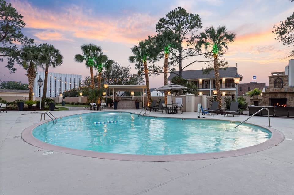Resort pool at dusk with palm trees, lounge chairs, fireplace, and lit gazebo