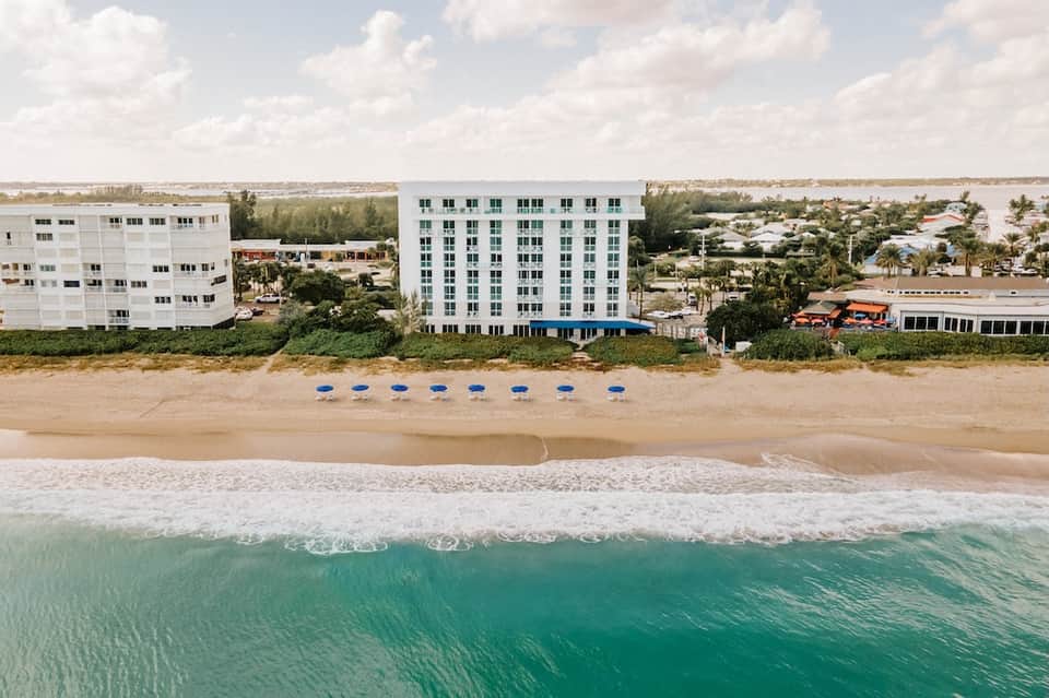 Beachfront resort building with white facade and blue umbrellas on sandy beach with ocean waves