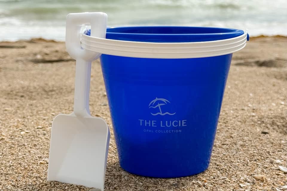 Blue branded bucket with shovel on beach sand near ocean waves