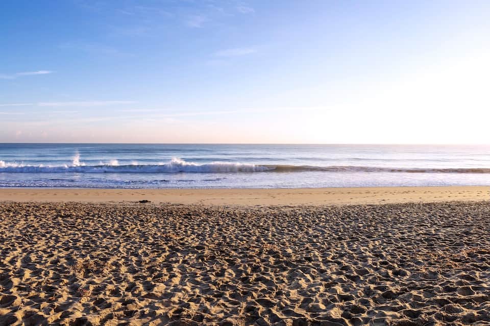 Sandy beach with waves, clear blue sky, and calm ocean horizon
