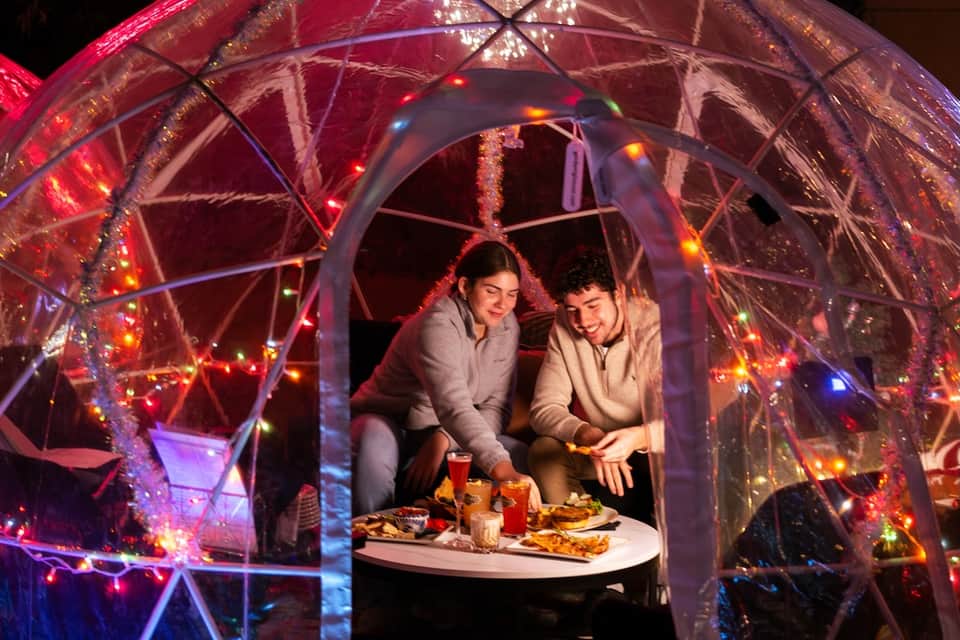 Illuminated outdoor dining pod with colorful lights and couple inside
