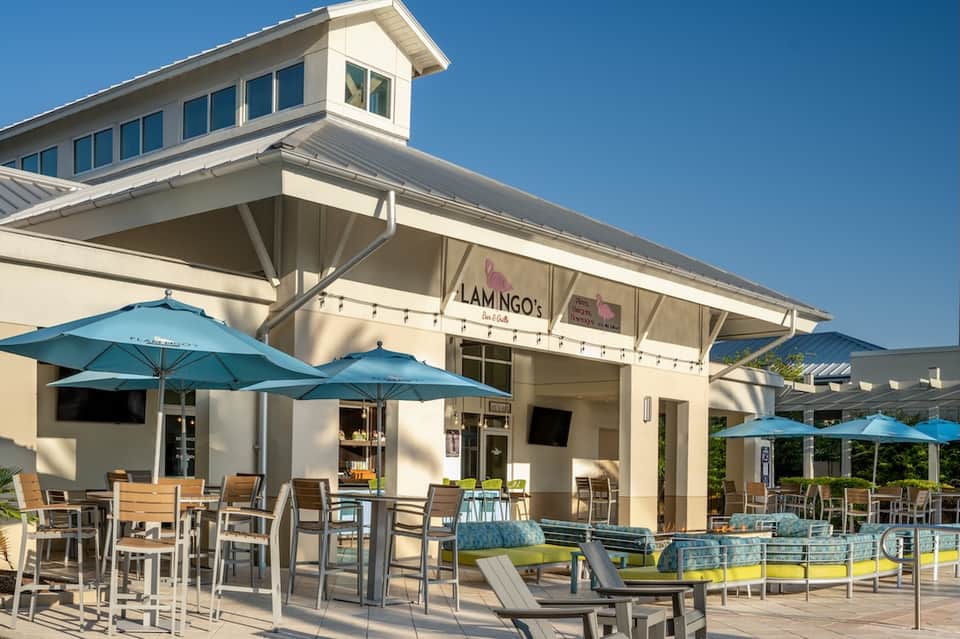 Casual beachside restaurant with blue umbrellas, outdoor seating, and sand dune access