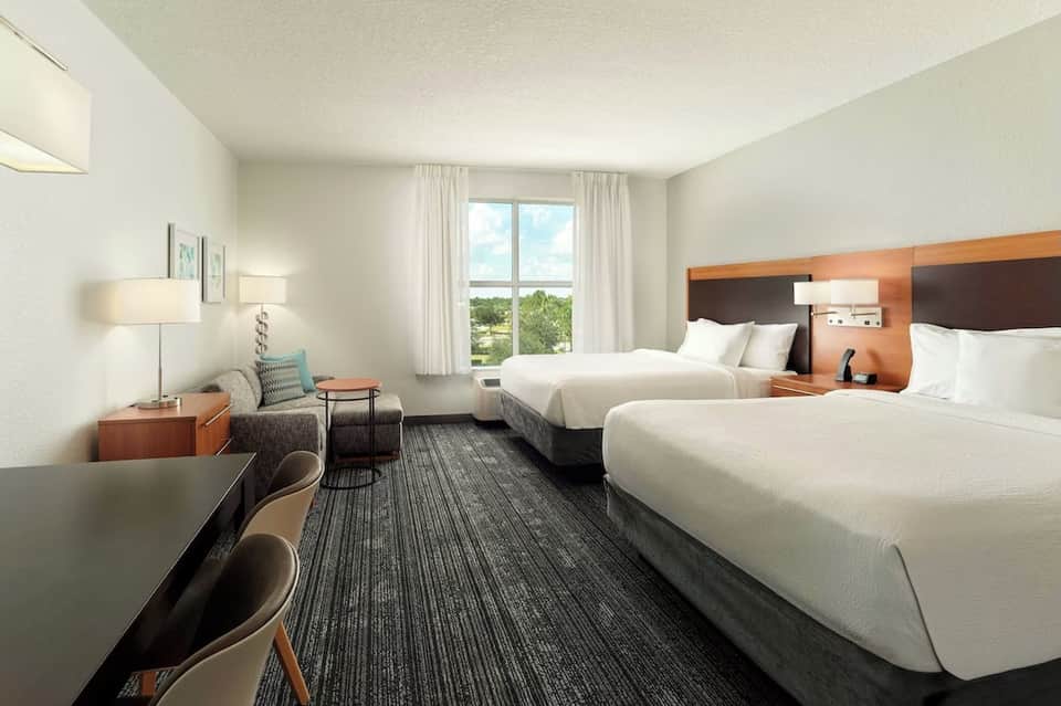 Modern hotel room with two queen beds, warm wood accents, and large window with scenic view