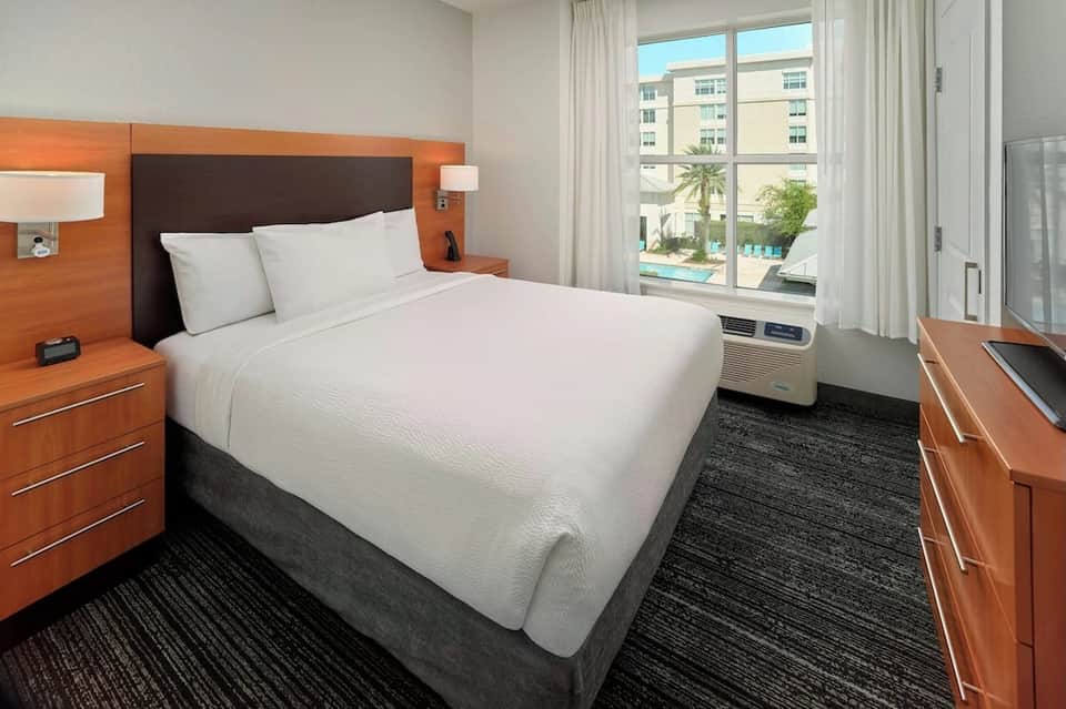 Hotel bedroom with orange headboard, white bedding, pool view, and modern furnishings