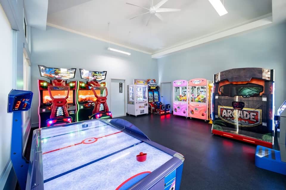 Hotel game room with air hockey table, arcade games, claw machines, and neon lighting