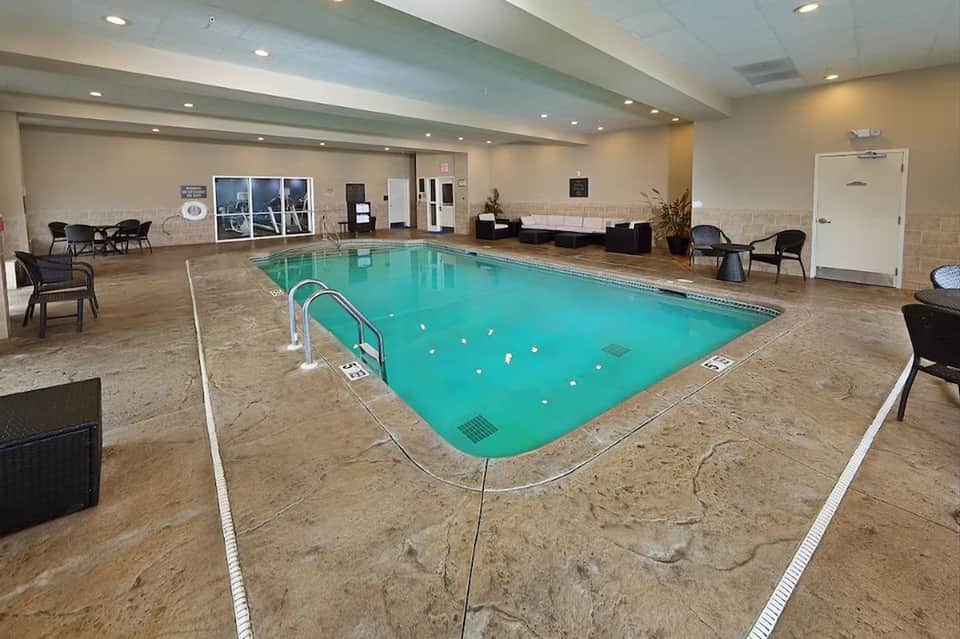 Indoor hotel pool with turquoise water, lounge seating, and contemporary ceiling design