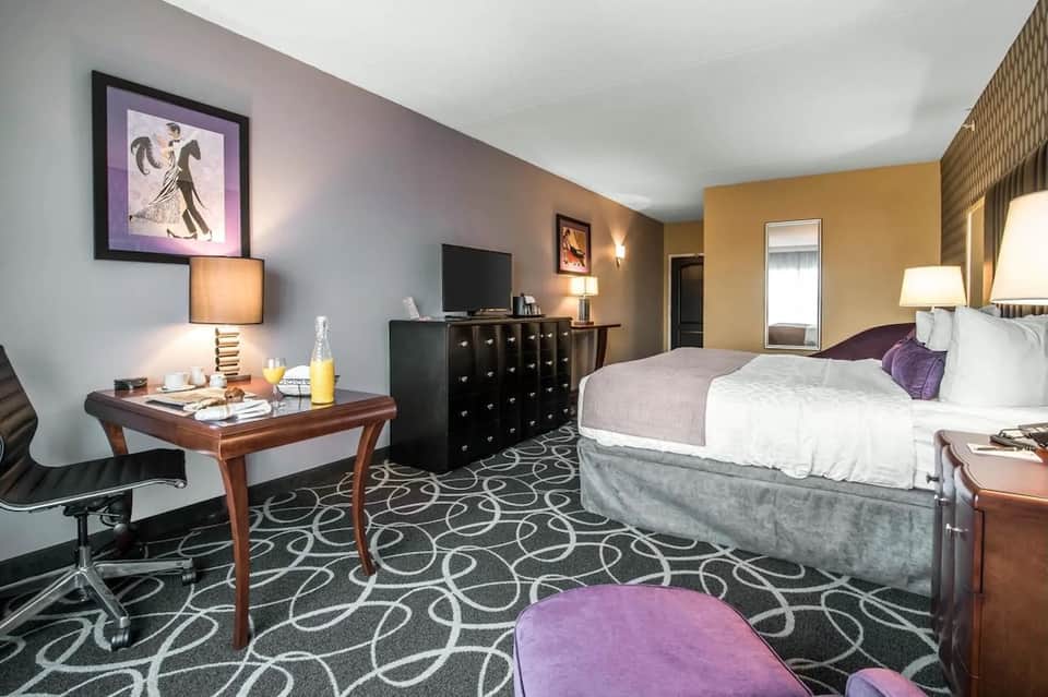 Hotel room with two beds, desk, TV, and purple and gold color accents