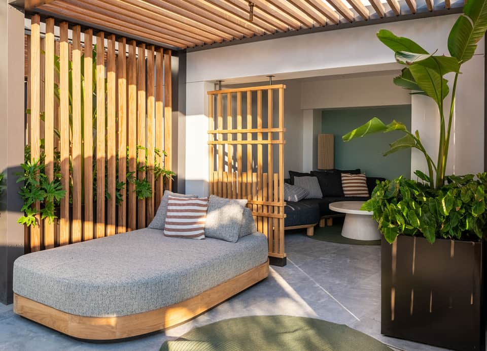 Modern outdoor lounge space with wooden pergola, daybed, plants, and contemporary furnishings