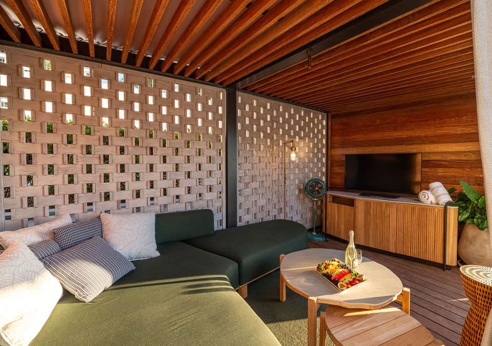 Outdoor living space with green sofa, wooden TV stand, brick pattern wall, and covered ceiling