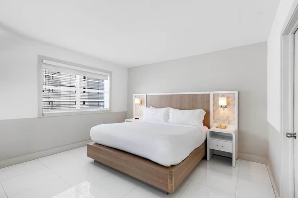 Modern hotel bedroom with queen bed, wood headboard, white linens, and window seating