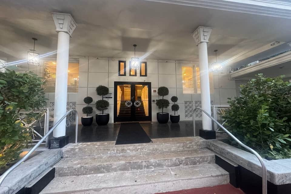 Elegant building entrance with white columns, black doors, and manicured topiaries