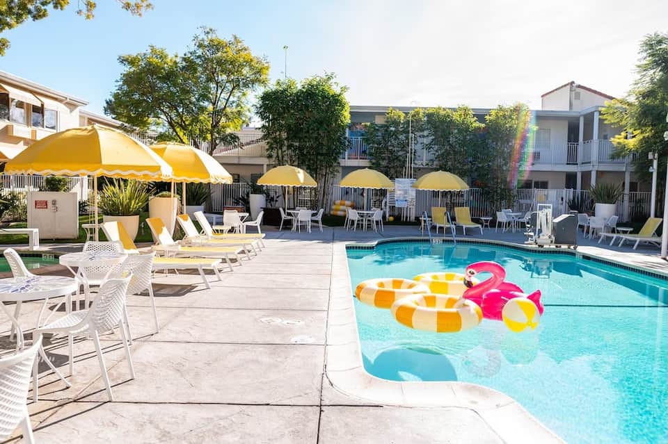 Daytime pool area with yellow umbrellas, white lounge chairs, and inflatable flamingo float toy