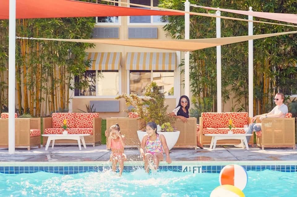 Resort pool with families swimming, woven lounge seating, and bamboo privacy screens