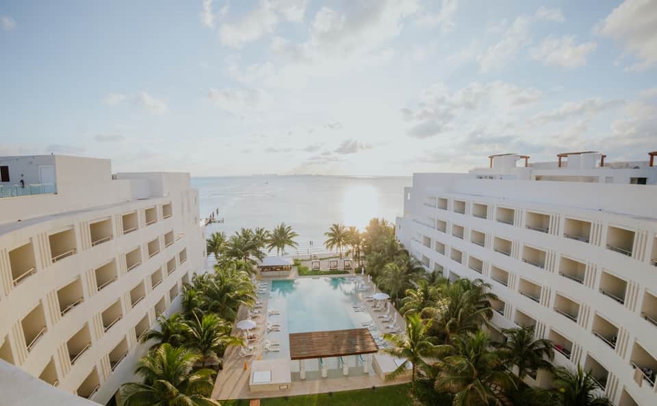 Beachfront resort aerial view with central pool, palm trees, and ocean backdrop