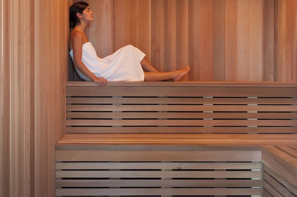 Woman in white towel relaxing in wooden sauna with vertical wood paneling