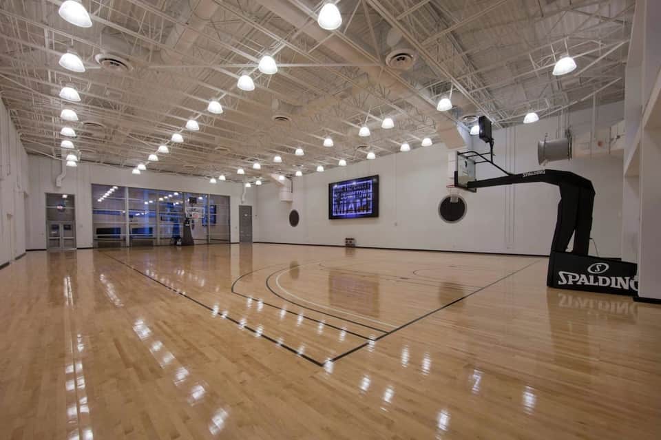 Indoor basketball court with wooden floor, bleachers, and bright overhead lighting