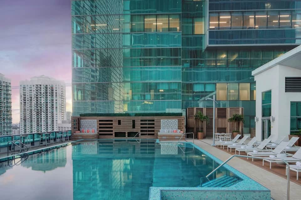 Rooftop pool at dusk with city skyline, lounge chairs, and modern architectural design