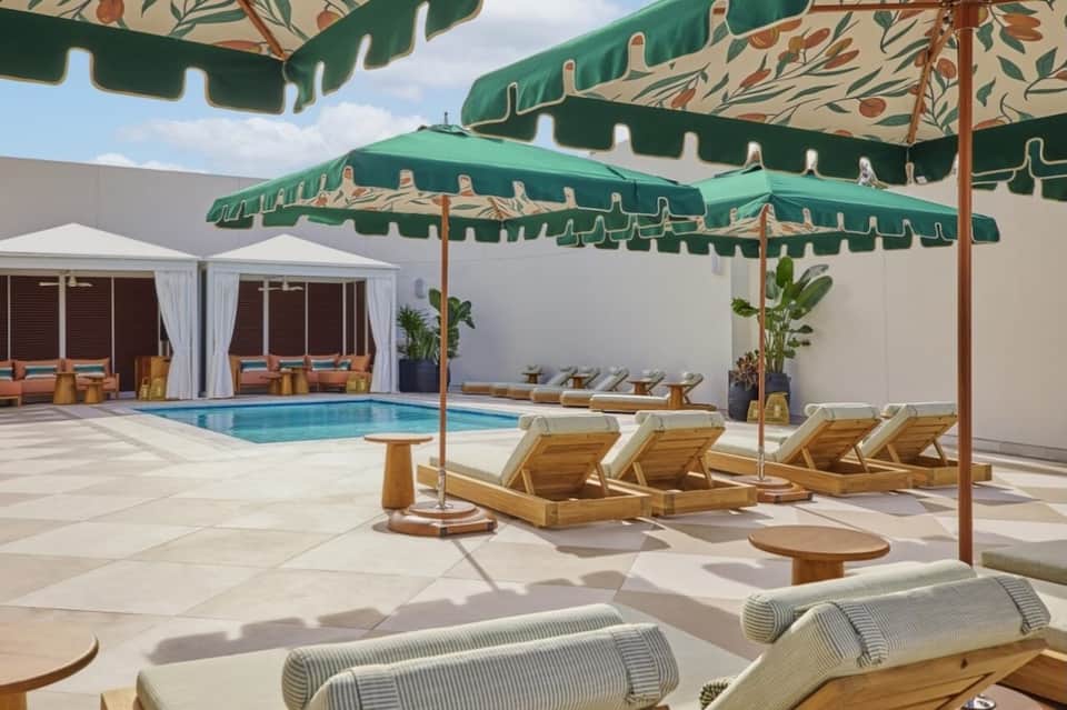 Luxury pool terrace with wooden loungers, green umbrellas, and cabana pavilions
