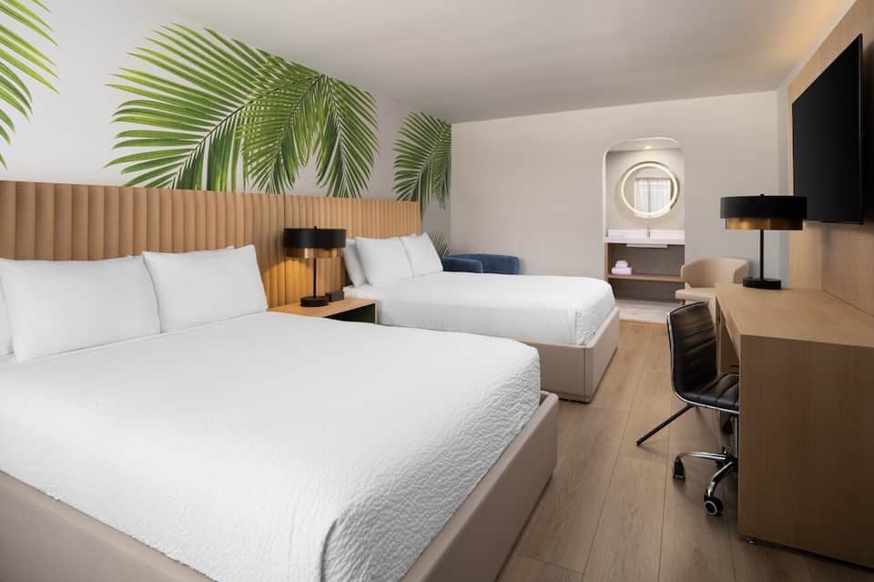 Modern hotel room with two queen beds, palm leaf headboard artwork, and contemporary furnishings