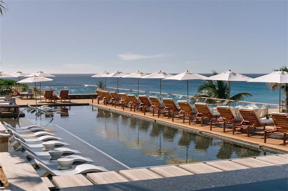 Beachfront infinity pool with ocean views, lounge chairs, and white umbrellas