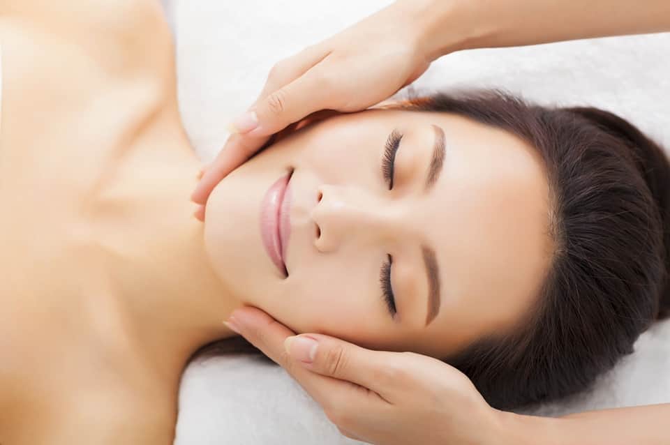Relaxing facial massage treatment with therapist's hands on client's face on white towel