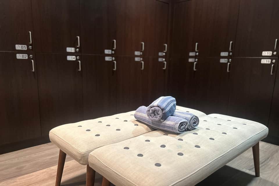 Spa changing room with towel rack, rolled towels on bench, and dark wood lockers