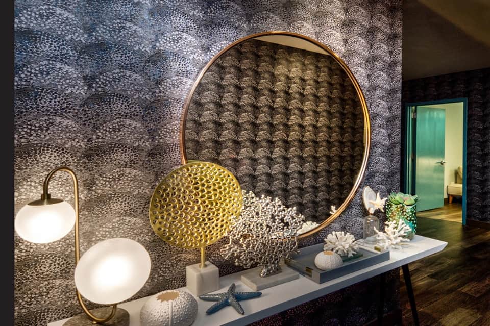 Luxury spa entrance with textured wall art, brass circular mirror, decorative objects, and ambient lighting