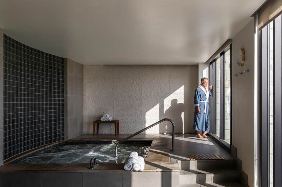 Spa area with sunken soaking tub, black tile wall, glass doors opening to patio, and natural light