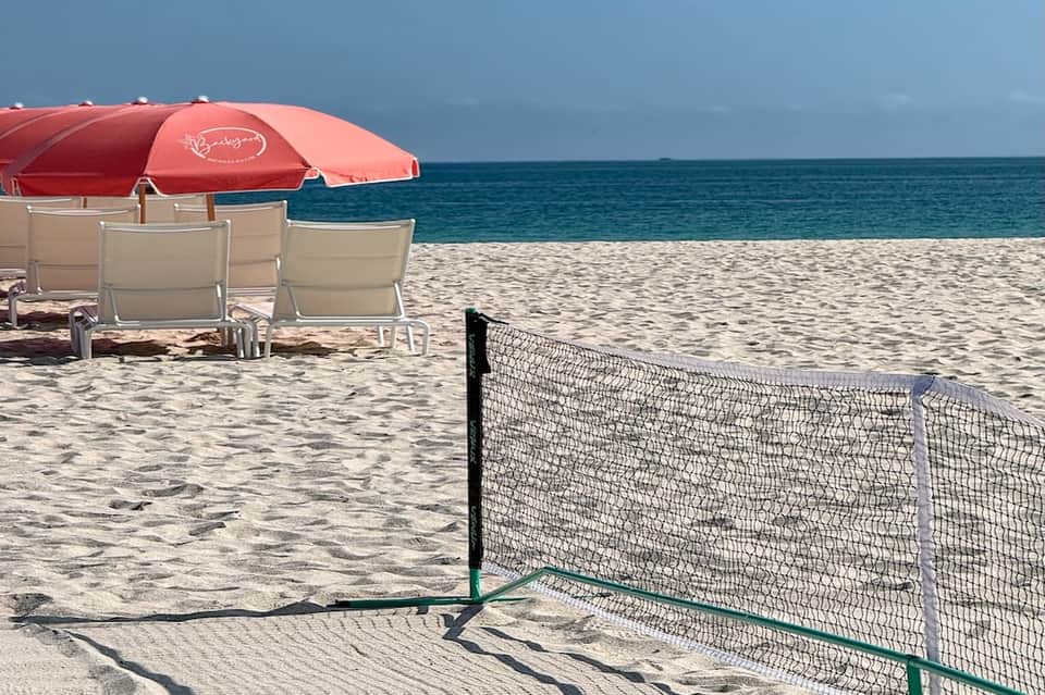 Beach scene with volleyball net, red umbrella, loungers, and ocean horizon