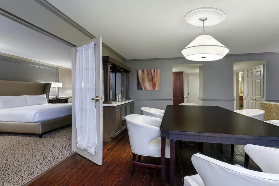 Luxury hotel suite with king bed, spa bath with soaking tub, dark vanity, pendant lighting, and elegant neutral decor