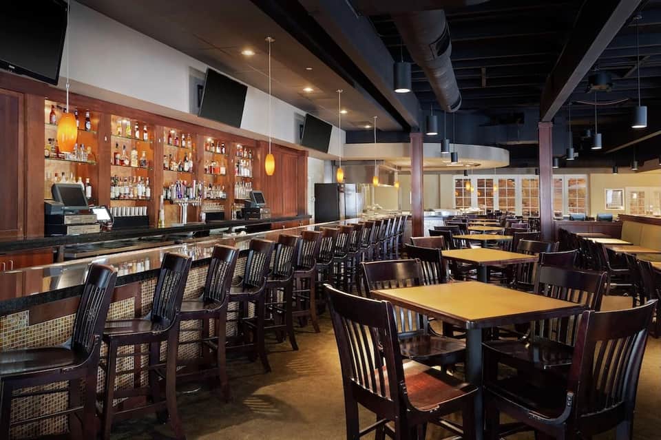 Resort bar and lounge with wooden bar counter, dark seating, and ambient pendant lighting
